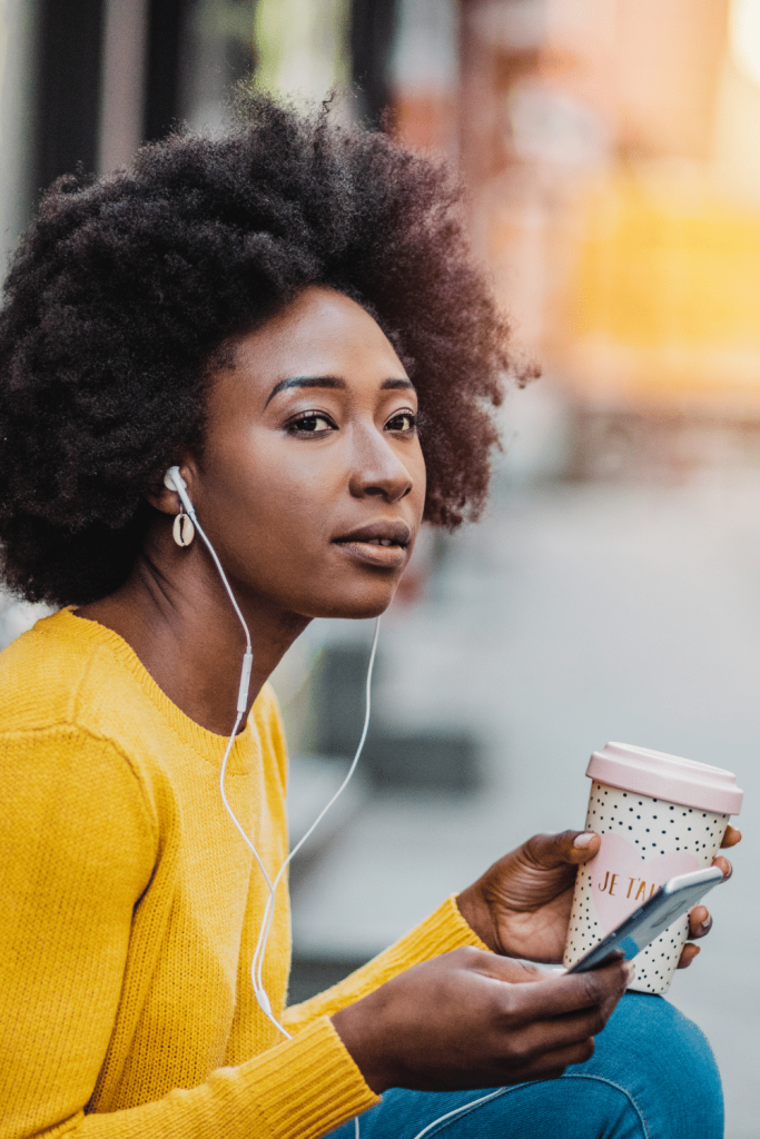 woman with earbuds, drinking a coffee