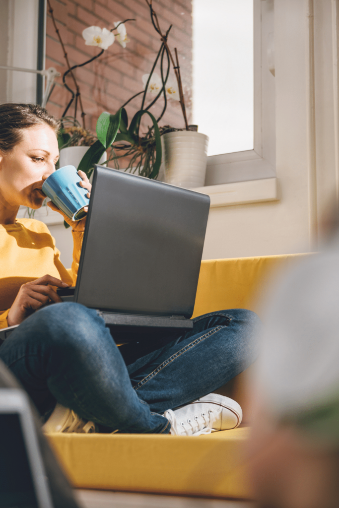 woman drinking from blue cup, holding laptop.
